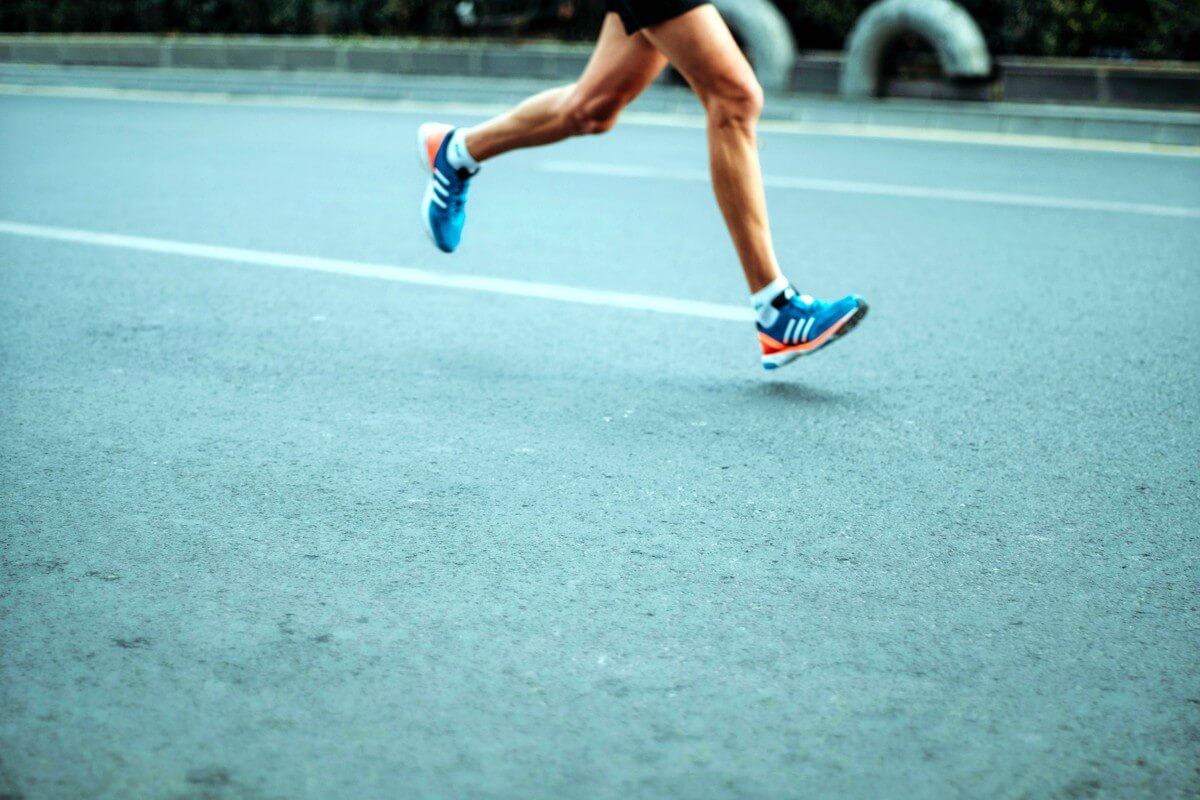 Ein Läufer mit blauen Laufschuhen auf dem Asphalt